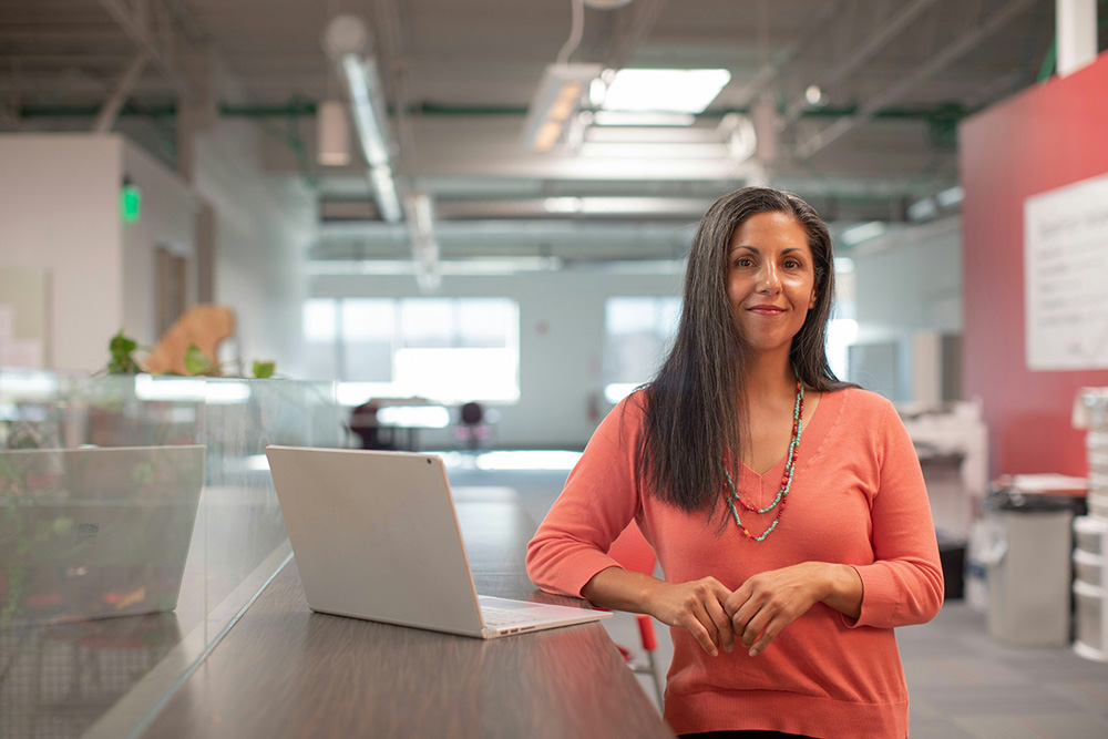 Woman in orange posing in front of a laptop